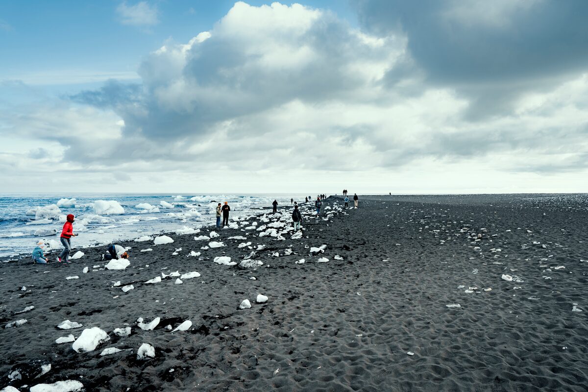 People walking among glacial ice pieces on Diamond Beach in Iceland. 