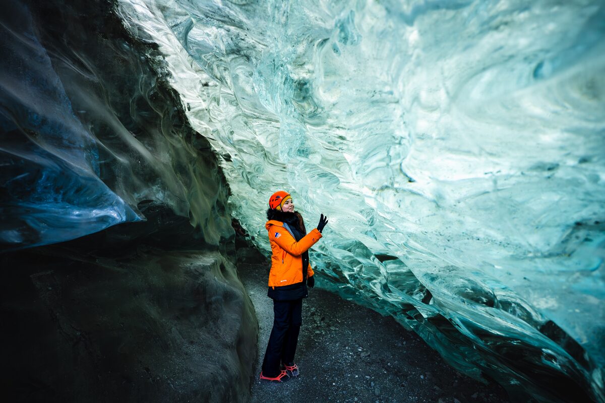 Woman in an orange jacket touching blue ice inside a crystal ice cave in Iceland.
