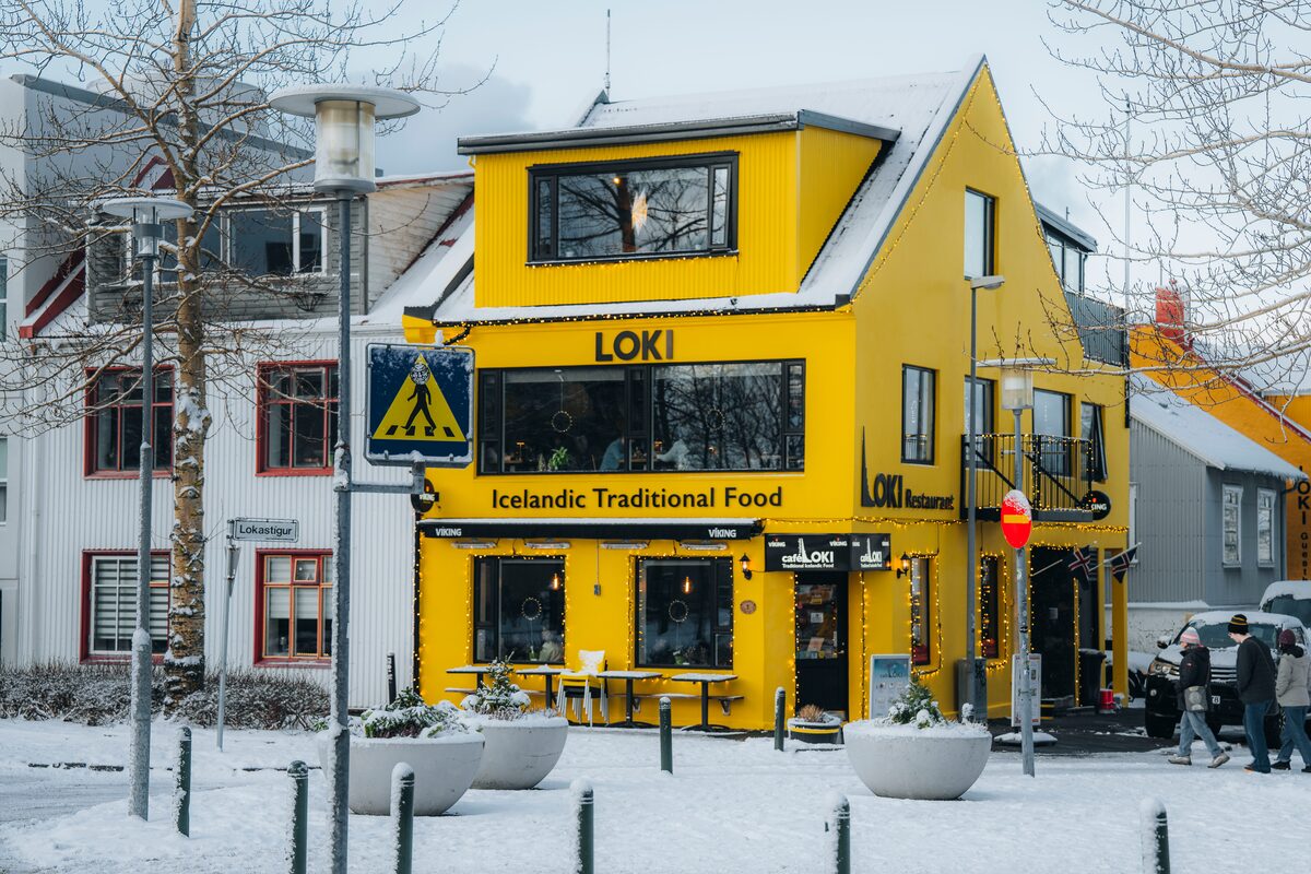 Yellow Kaffi Loki building in Reykjavík on a snowy day, with people walking past the entrance. 