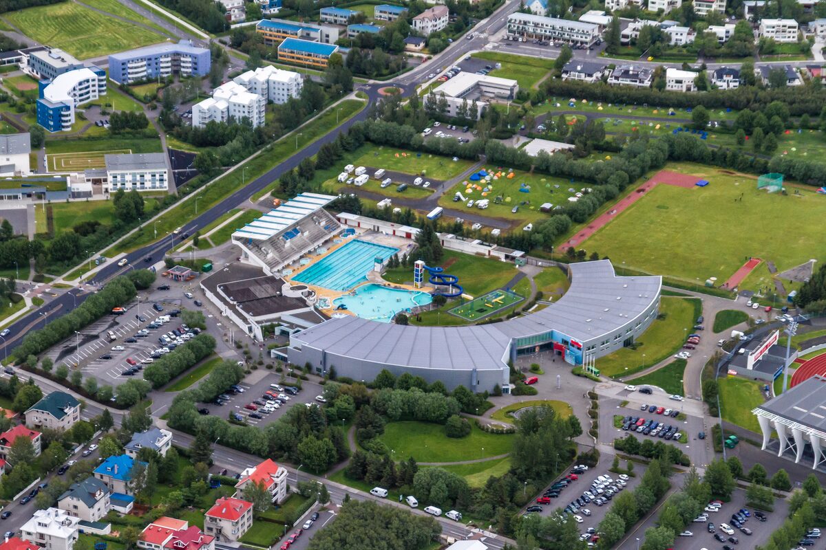 Aerial view of a swimming pool complex with outdoor pools, waterslides, and surrounding streets.