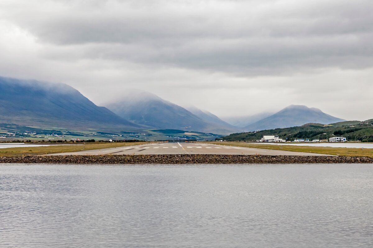 Runway at Akureyri Airport with mountains in the background under a cloudy sky.