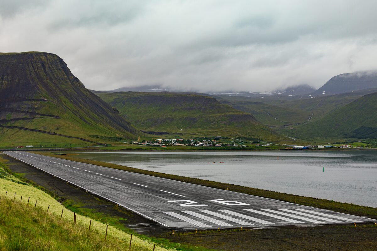 Runway at Ísafjörður Airport beside a fjord, with green mountains under low clouds.