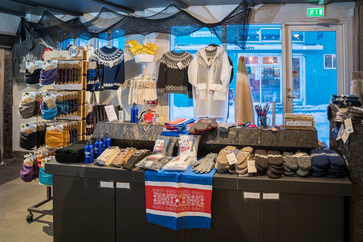 Display of lopapeysa sweaters and Icelandic wool accessories on tables and shelves inside a shop.