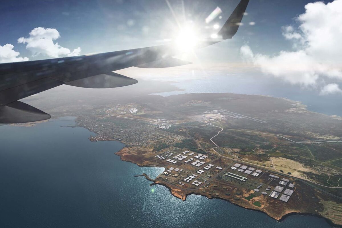 View from an airplane window over a coastline, with the wing and sun above scattered clouds.