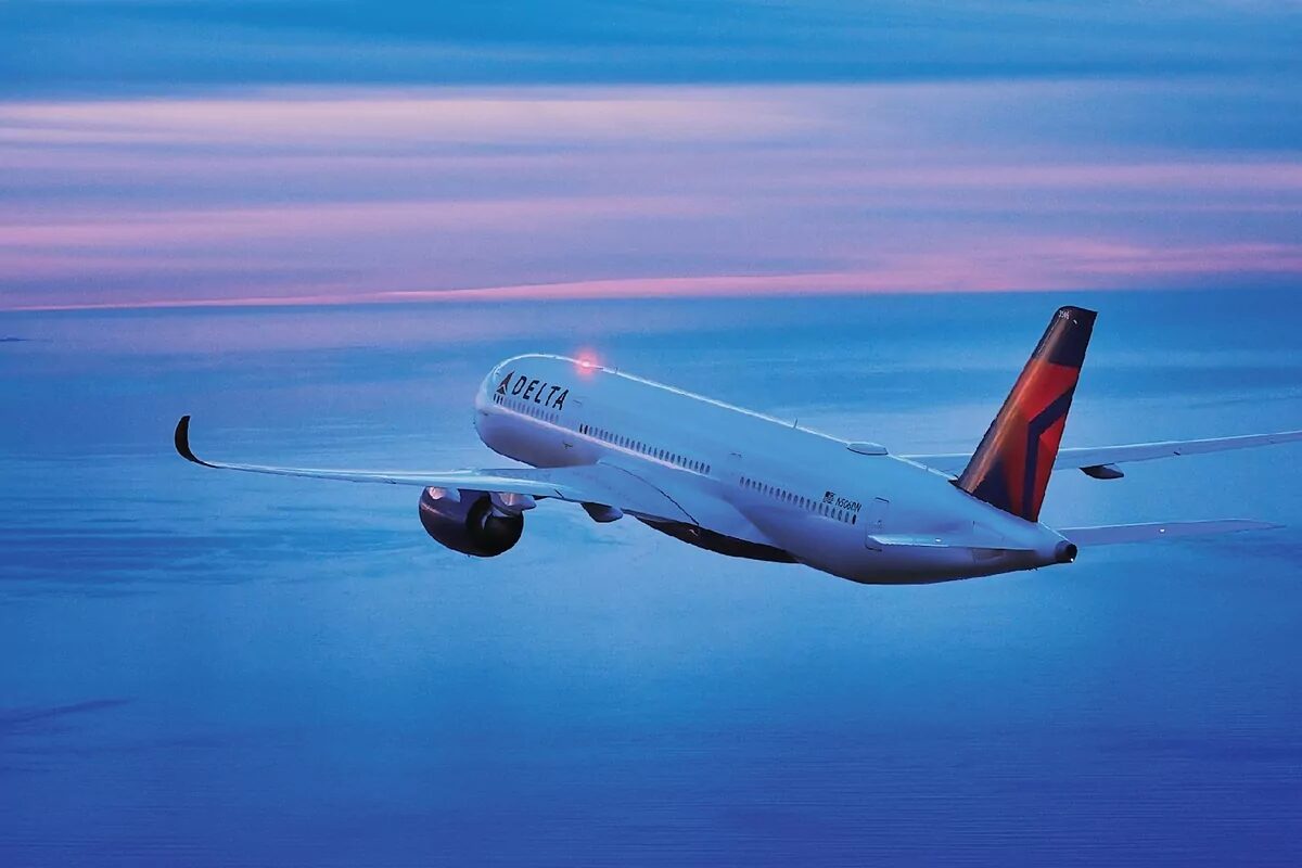 Delta airplane flying above the ocean at dusk with a pink and blue sky.