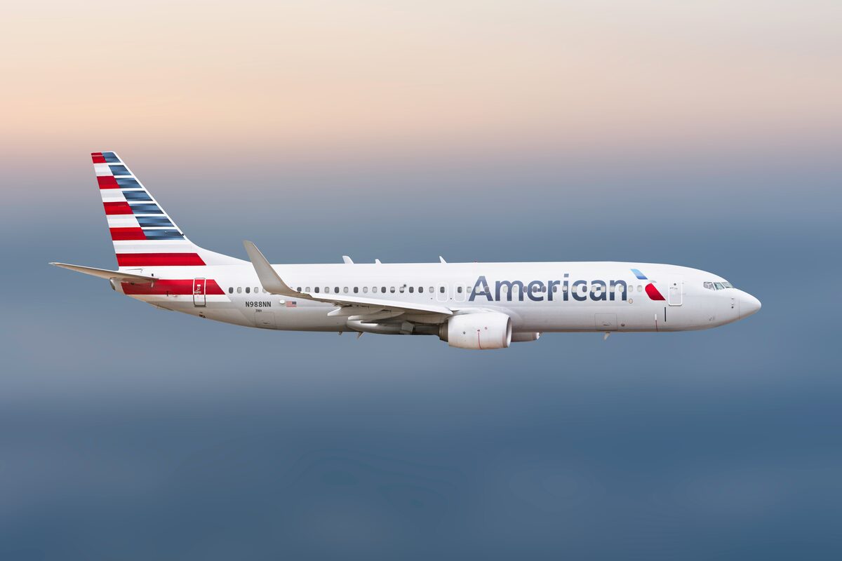 American Airlines airplane flying against a pale sky.