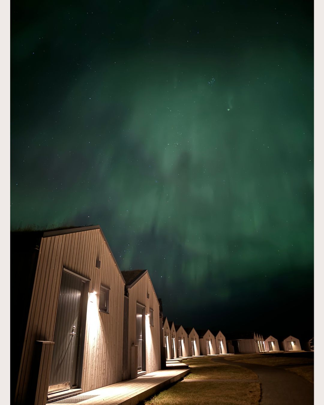 Cabins at Magma Hotel in South Iceland beneath the Northern Lights at night.