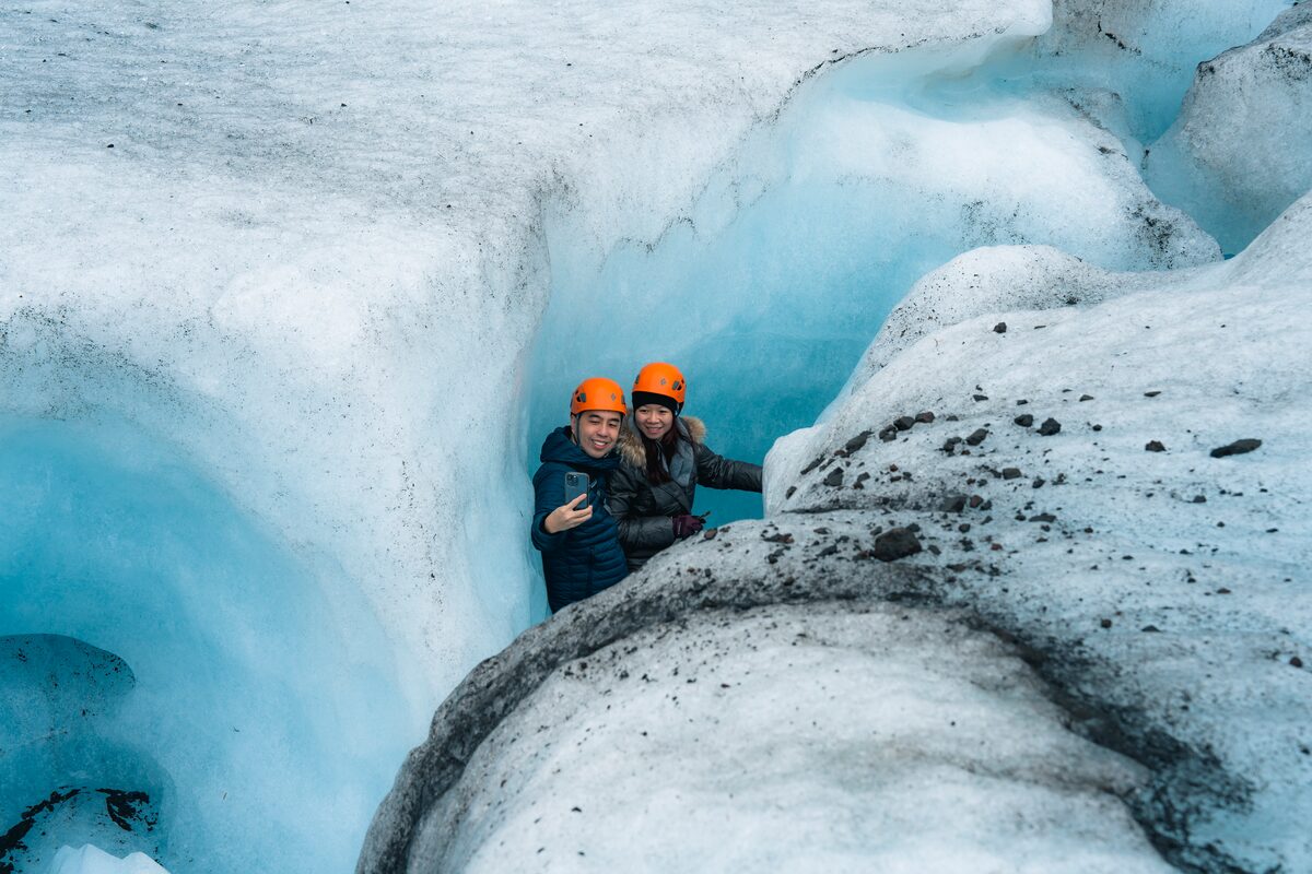 Couple in orange helmets taking a photo in the blue ice