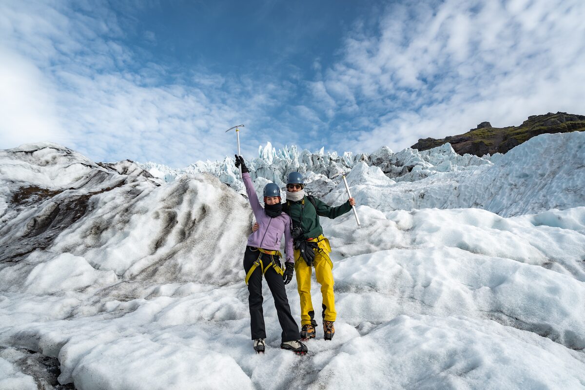 Two guests with dramatic icefall and blue sky in background, posing with ice axes up.