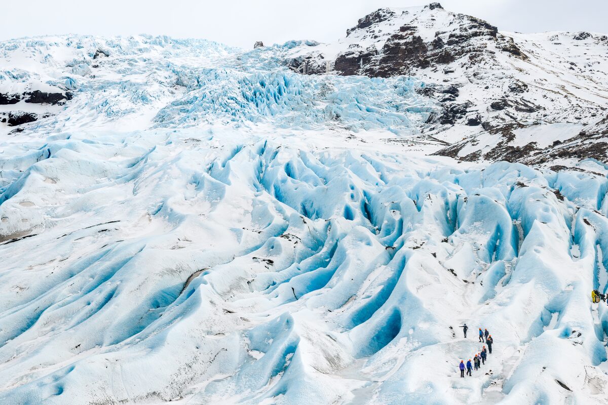 Distance shot of glacier with blue ice crevasses and a group looking small by scale