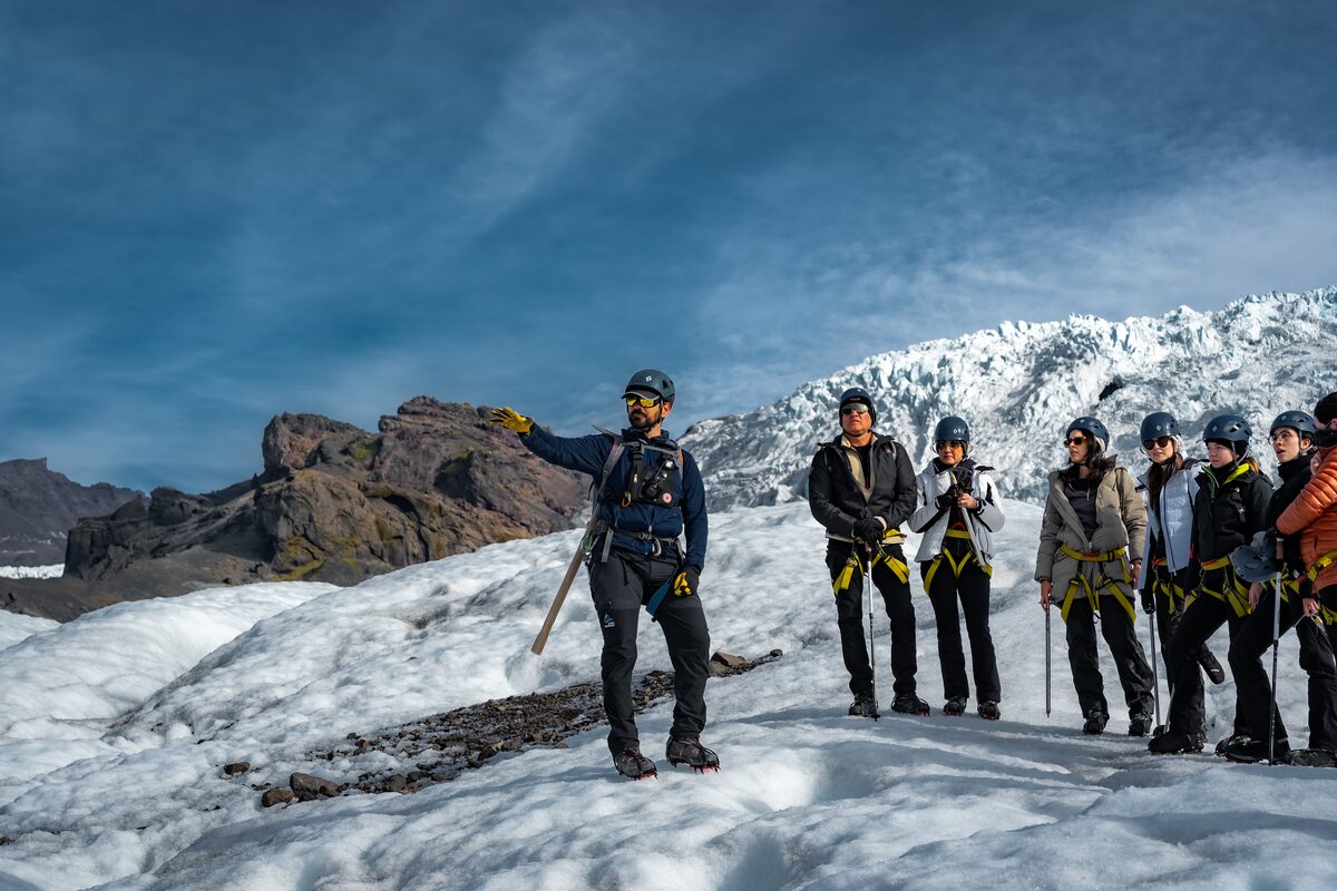 Guide pointing out glacier freature to group of guests with blue sky and icefall behind them