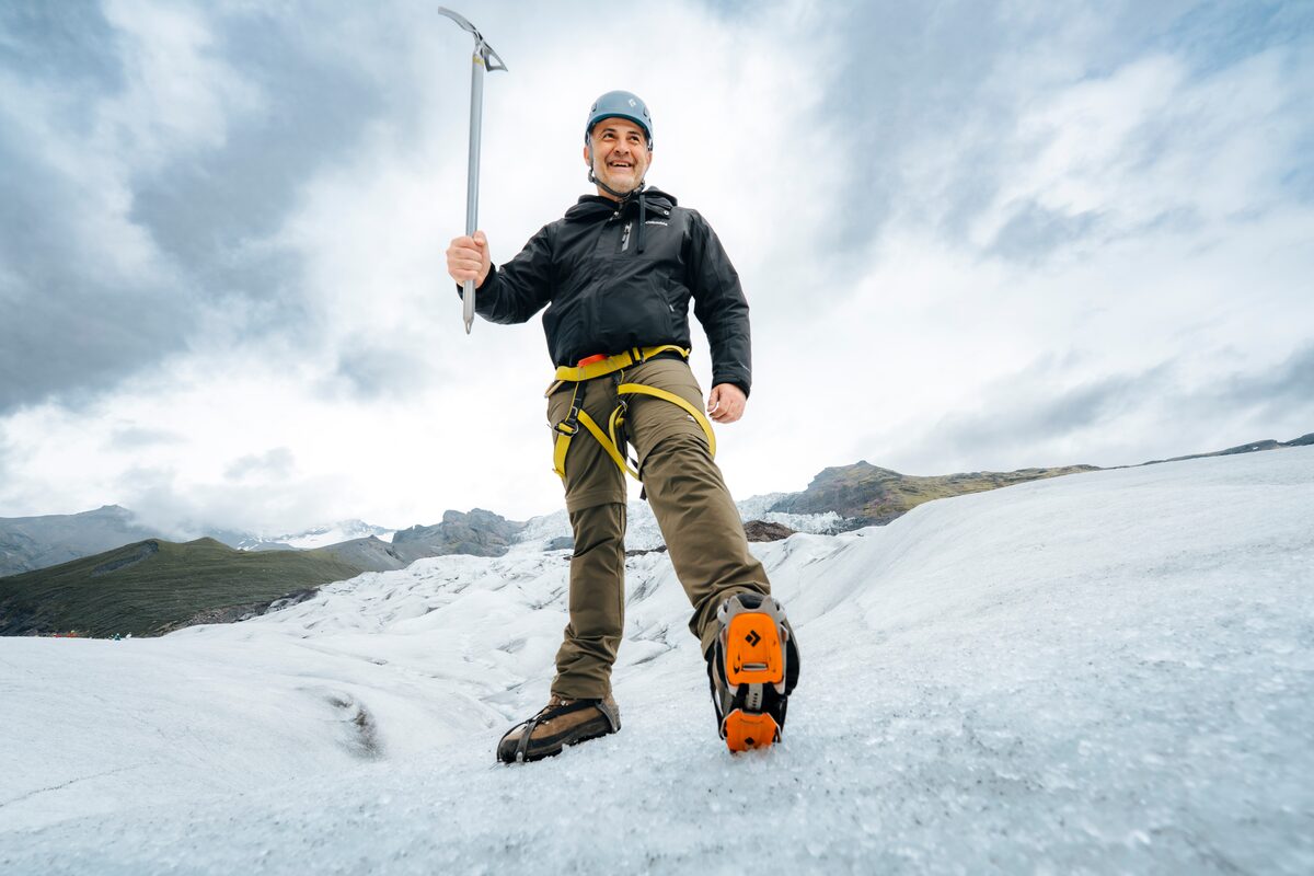 Smiling man posing with crampon out holding ice axe – geared up and ready to hike