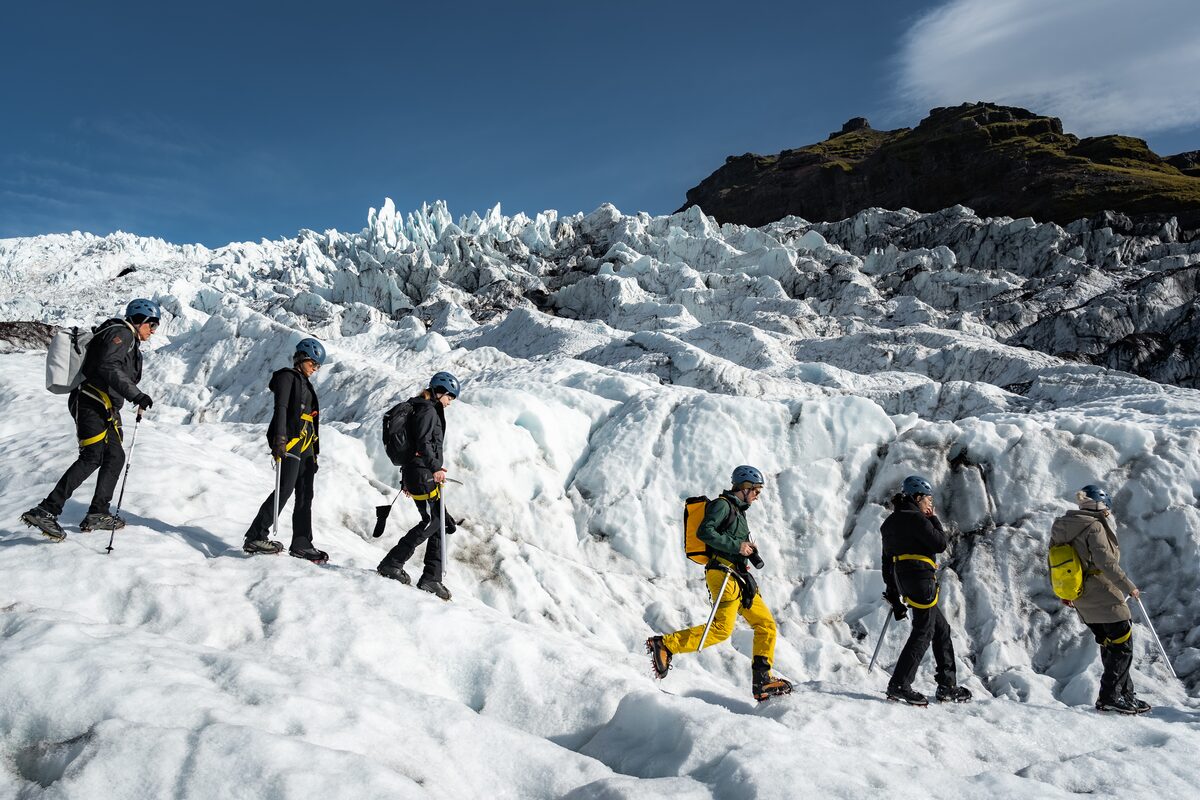 Group of guests walking down the glacier with jagged white peaks behind them