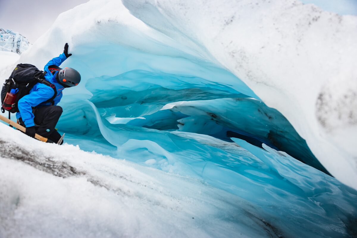 Man in blue jacket looking at blue ice hole in Iceland