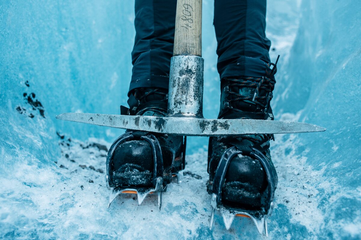 Close up of glacier crampons on boots and ice axe surrounded by blue ice