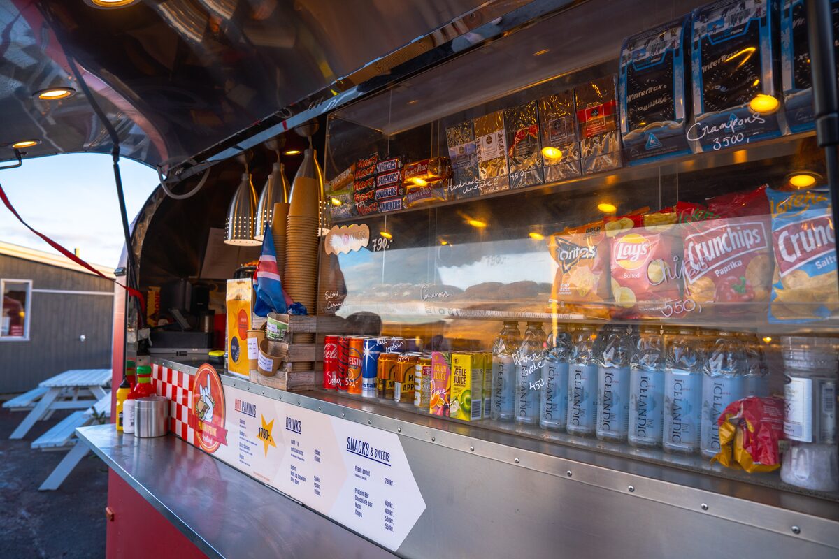 Kerid food truck counter with snacks, drinks, and menu signs, with an Icelandic flag inside.