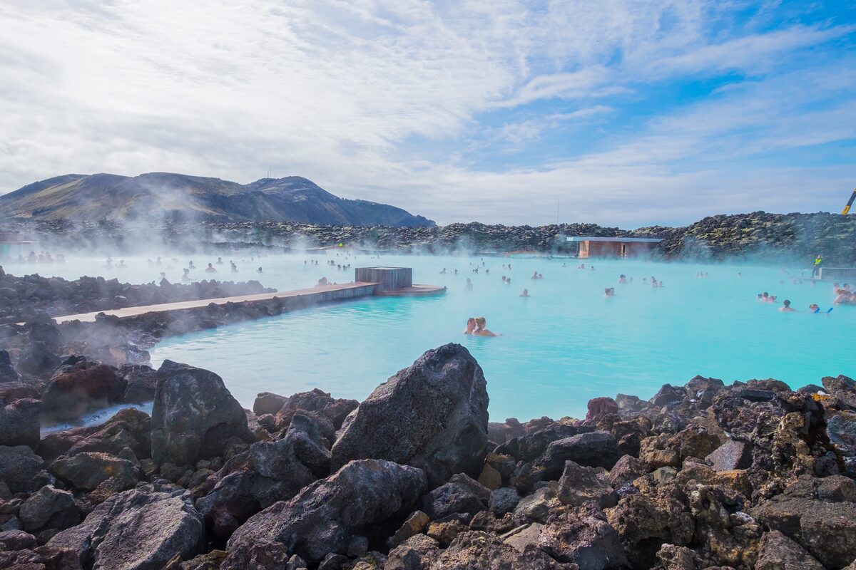 Wide view of the Blue Lagoon in Iceland with milky blue water, steam, and lava rocks.