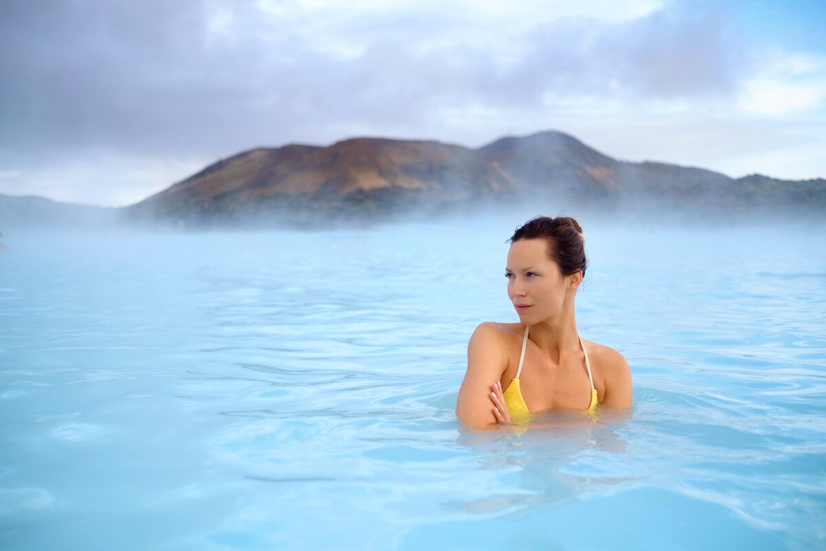Woman soaking in the Blue Lagoon in Iceland with mountains in the background.