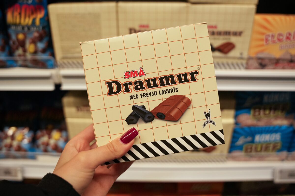 Hand holding a box of Smá Draumur chocolate-covered licorice candy in a store.