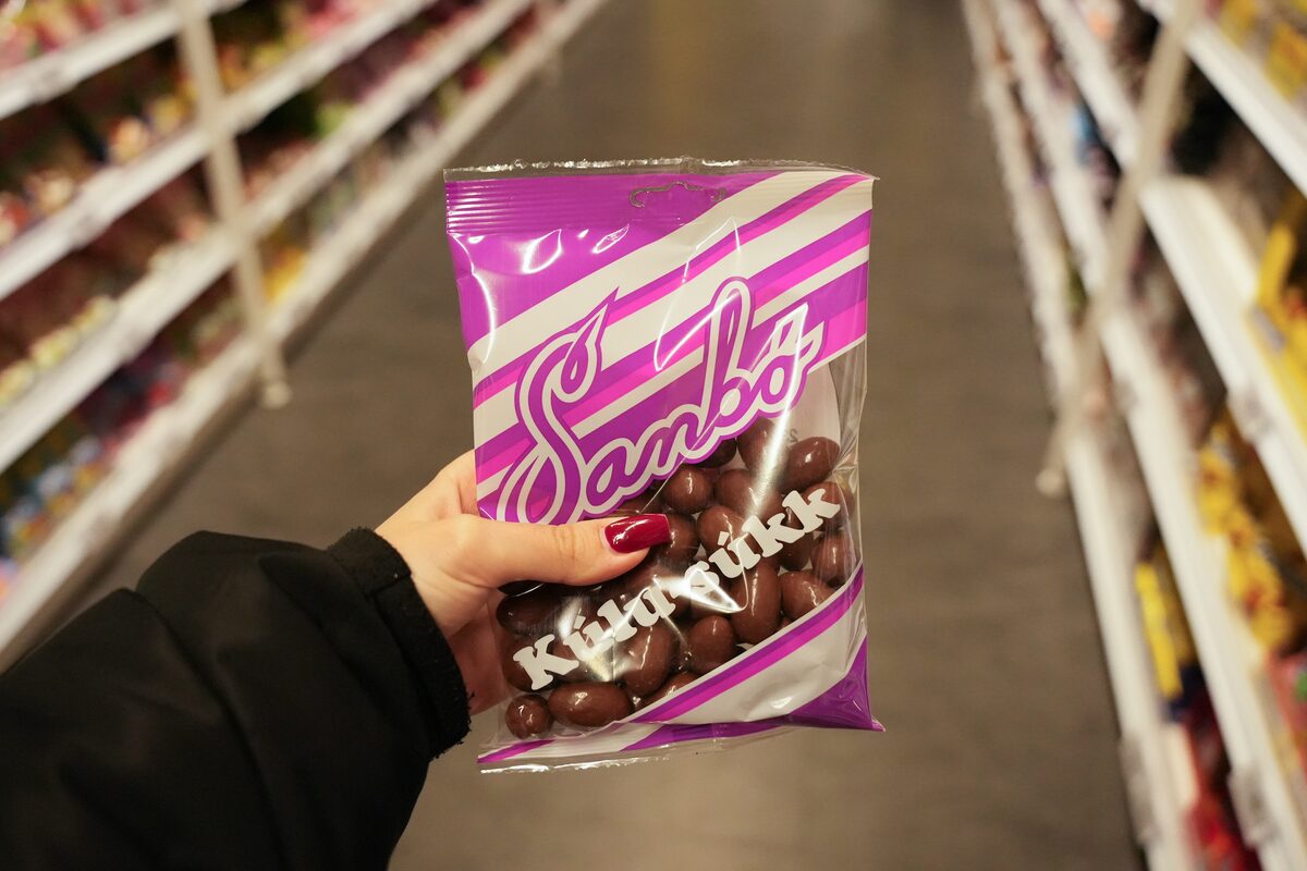 Hand holding a pink and white bag of Kúlusúkk chocolate-coated licorice pieces in a store.