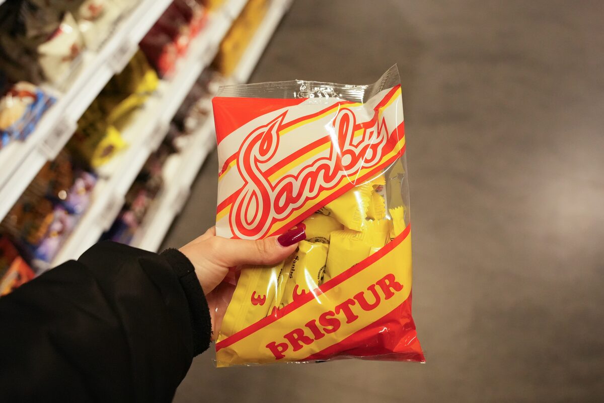 Hand holding a yellow bag of Sambó Þristur chocolate and licorice candy in a store aisle.