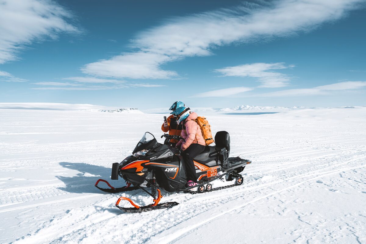 Rider on a snowmobile crossing a wide, snow-covered glacier in Iceland.
