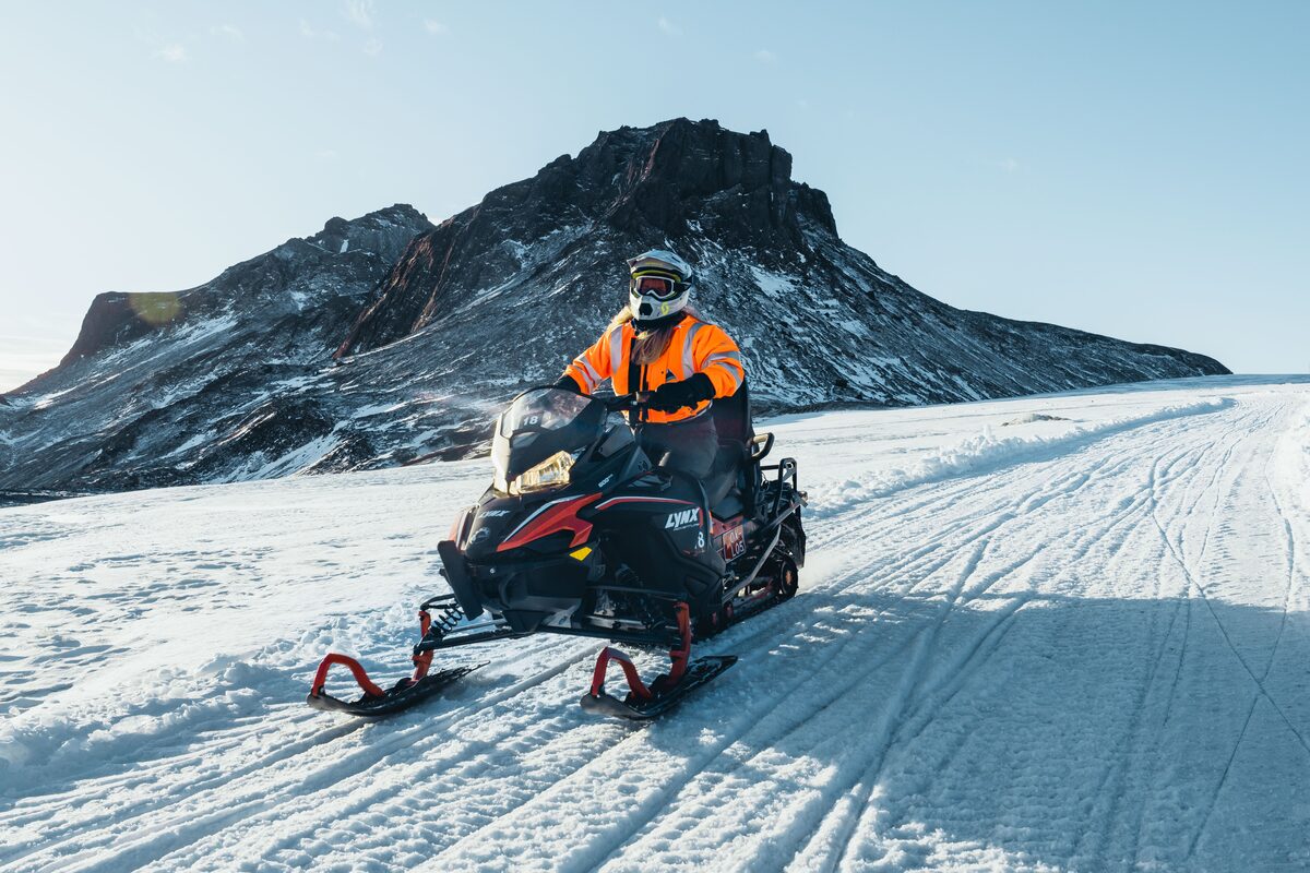 Rider on a snowmobile in an orange suit on a snowy glacier in Iceland.