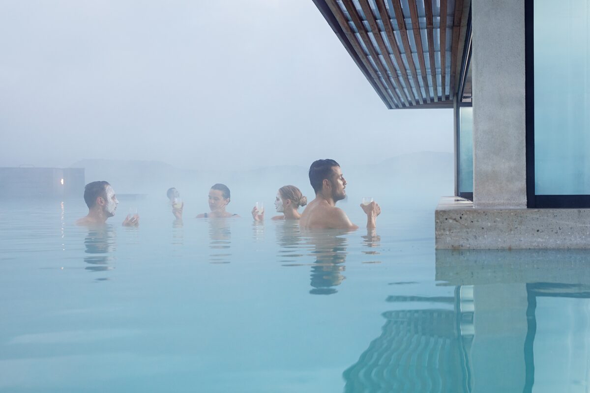 Group of people relaxing in a geothermal pool beside a modern concrete and wood structure, Iceland.