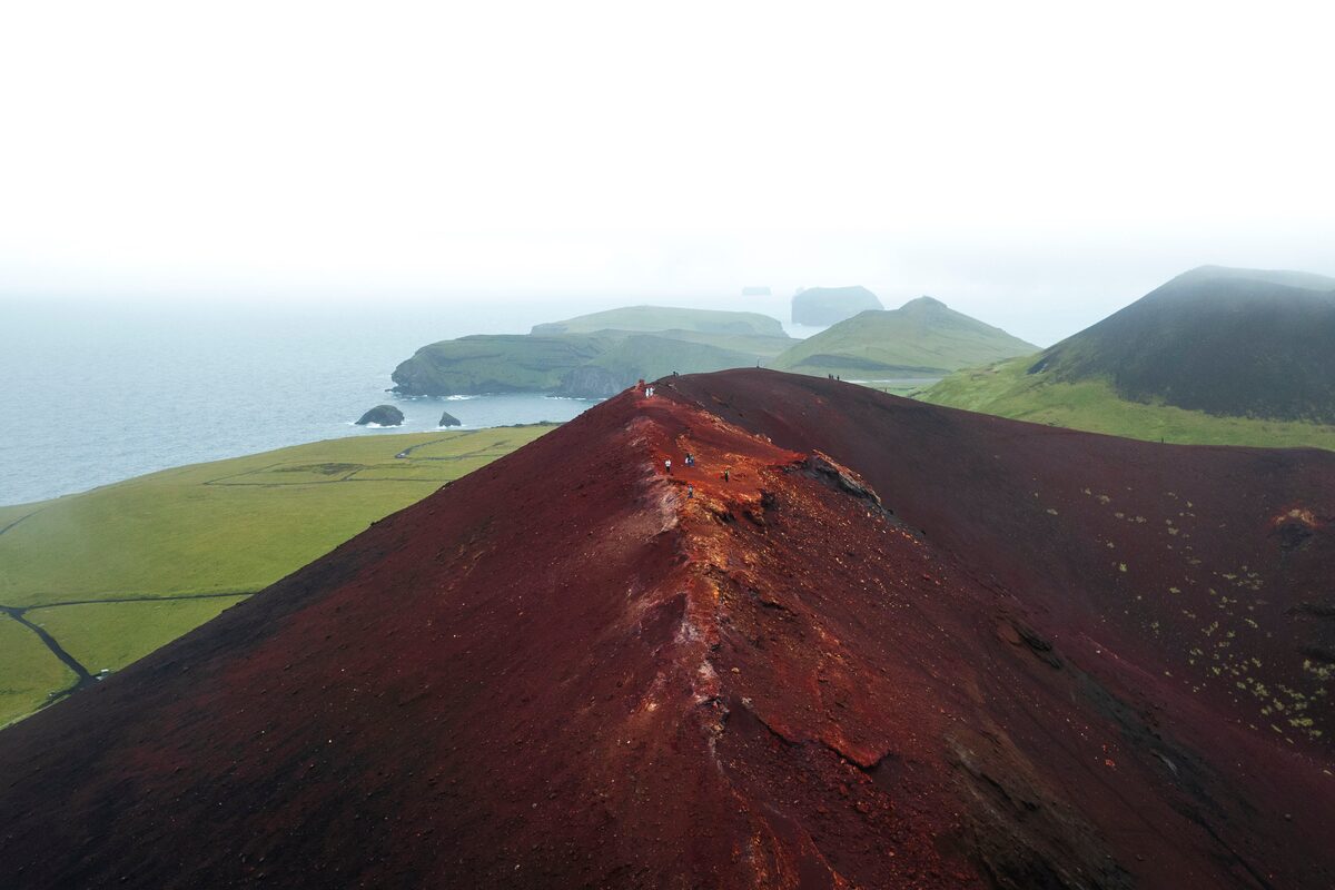 View along the red volcanic ridge of Eldfell crater on Heimaey, with the Westman Islands visible in the distance.