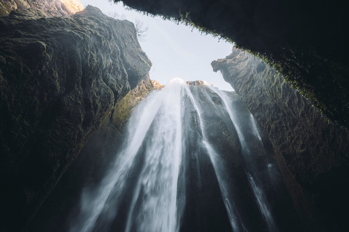 View from inside Gljúfrabúi gorge looking up at a waterfall cascading through mossy rock walls in South Iceland.