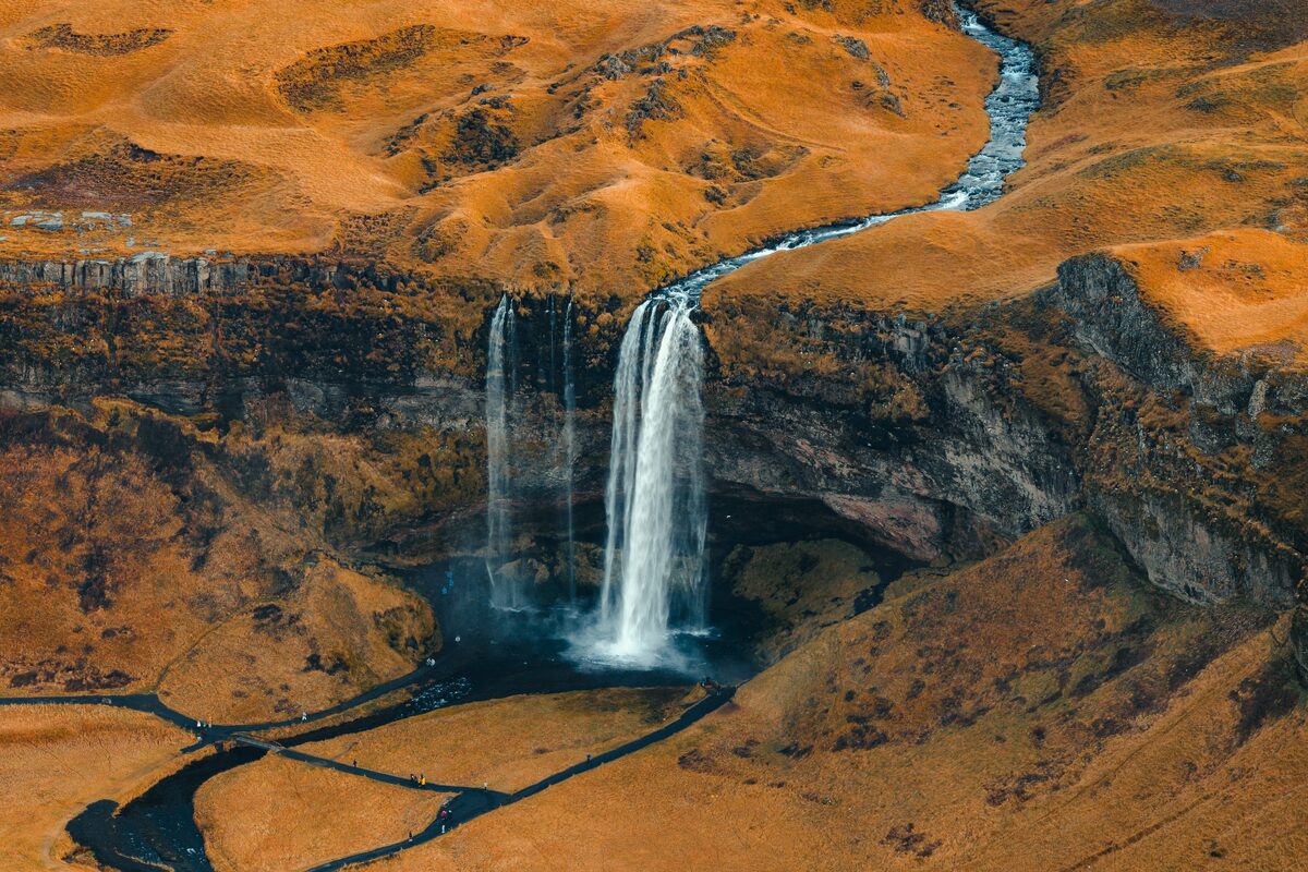 Aerial view of Seljalandsfoss waterfall dropping off golden cliffs in South Iceland, with a river winding below.