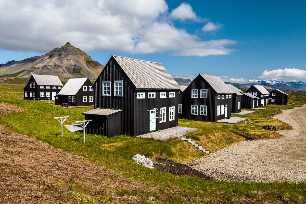 Black timber houses at Hellnar with a mountain peak rising behind them, Snæfellsnes Peninsula.