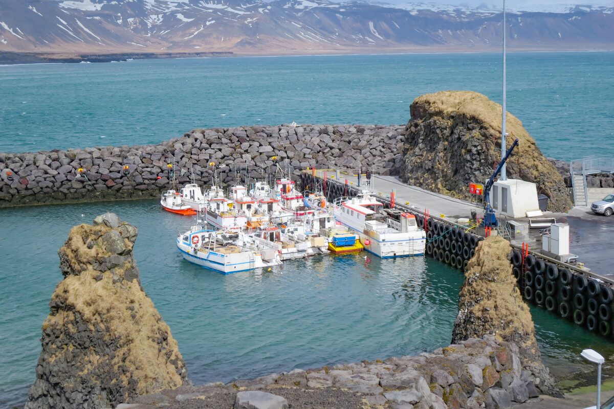 Small boats moored at Hellnar harbor behind a stone breakwater, Snæfellsnes Peninsula, Iceland.