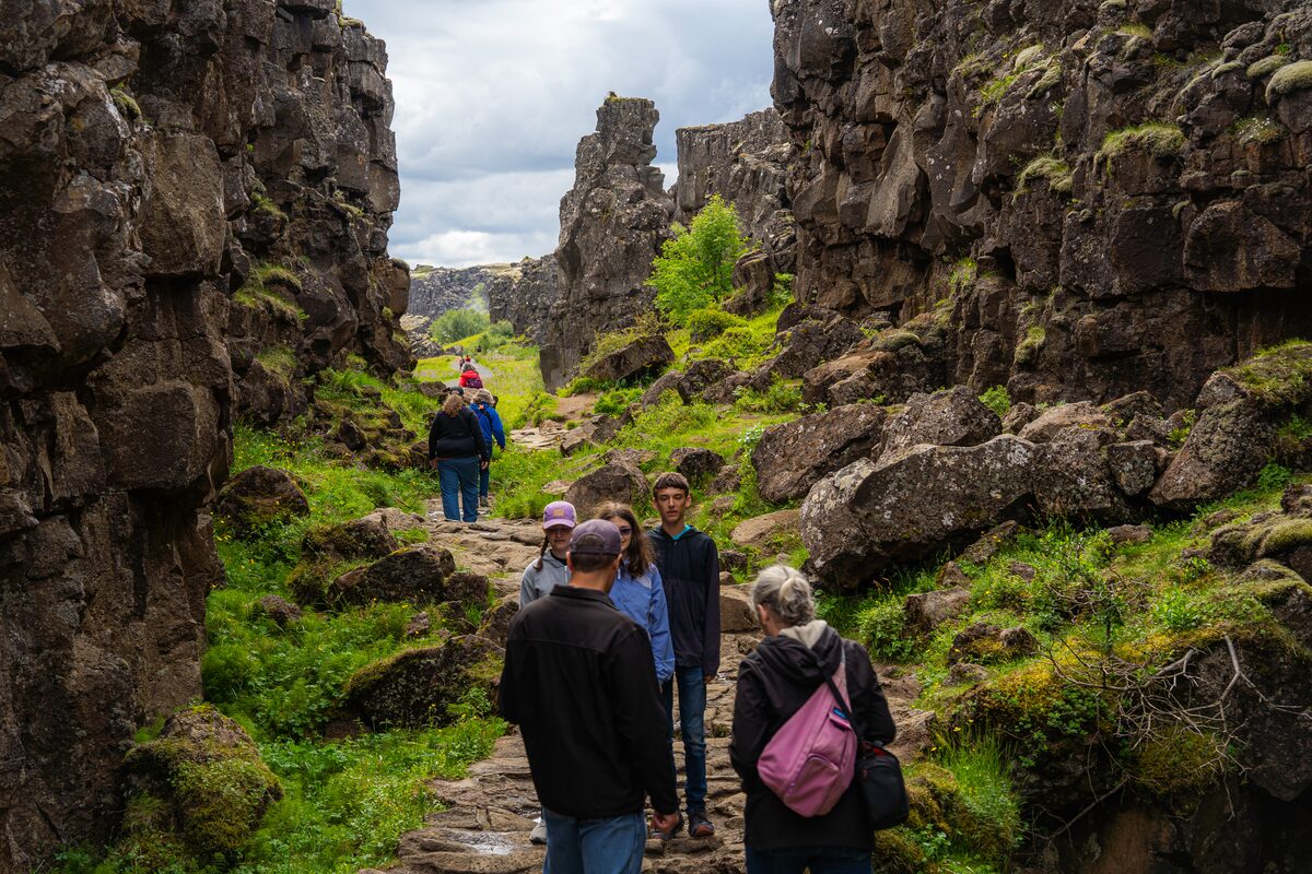 People walking through Þingvellir's rift between tall basalt cliffs.