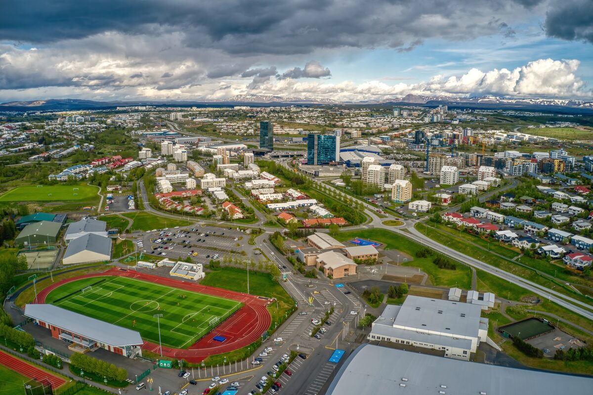 Aerial view of Kópavogur with Smáratorg Tower and Kópavogsvöllur stadium under cloudy skies.