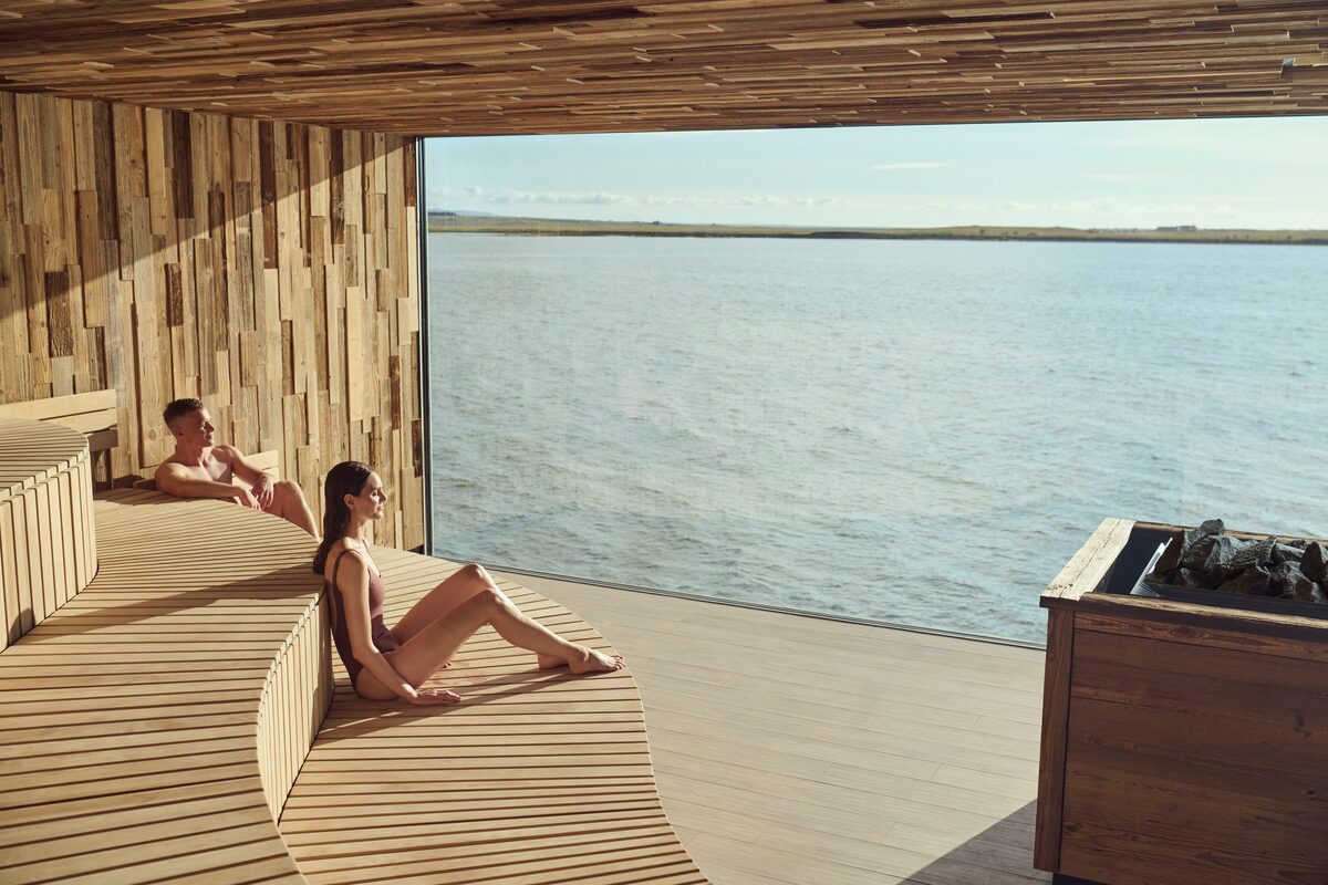 Two guests in Sky Lagoon's sauna with a floor-to-ceiling window facing the North Atlantic.