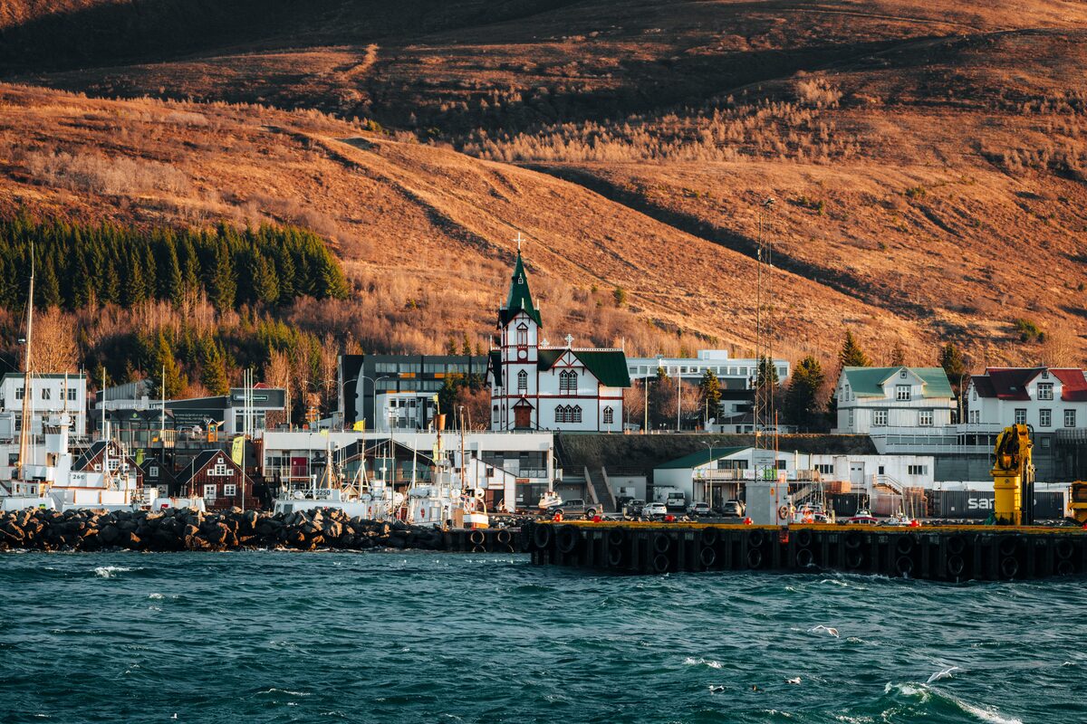 Húsavíkurkirkja church and Húsavík harbor with Húsavíkurfjall hill rising behind in evening light.