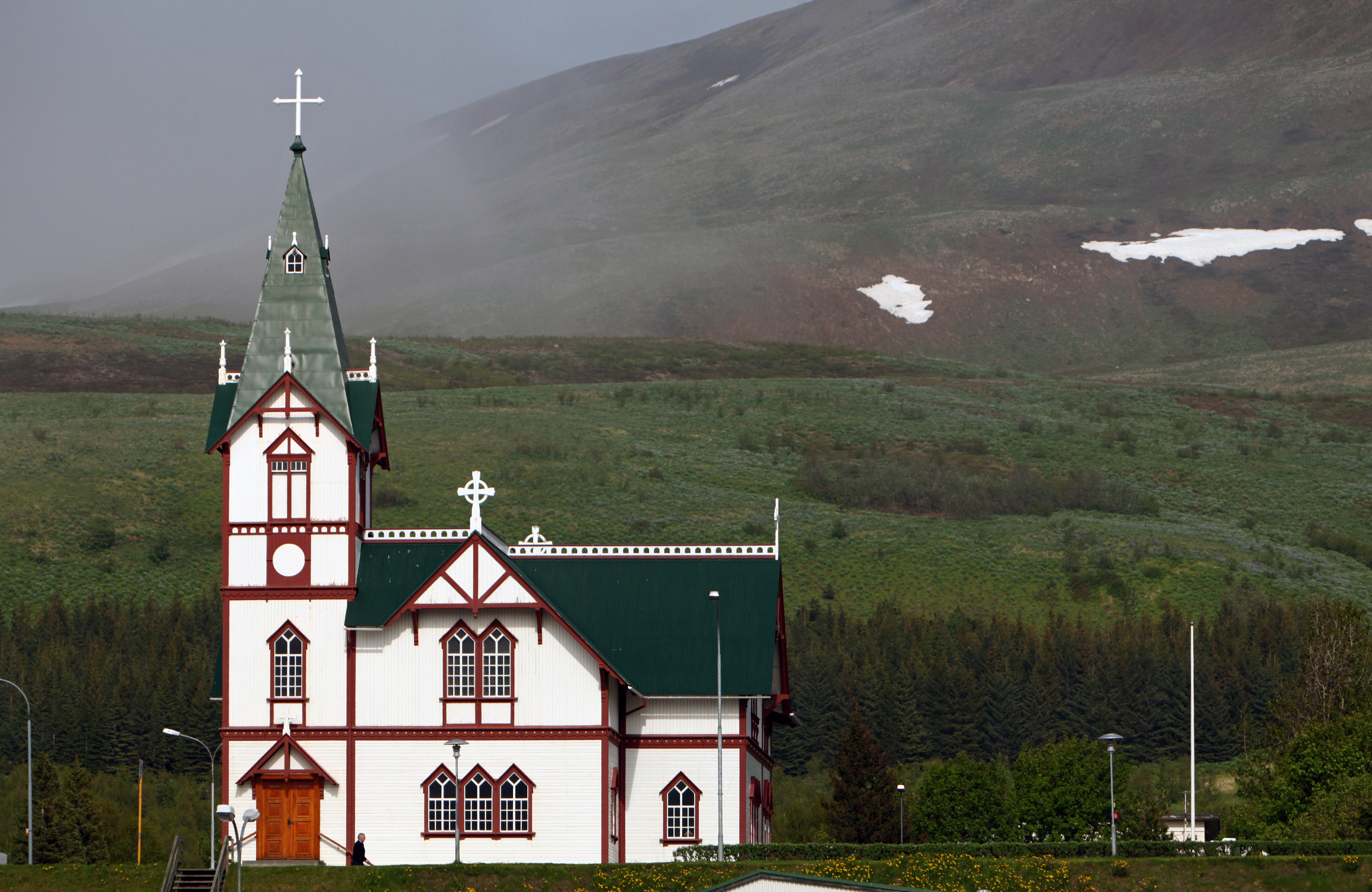 Húsavíkurkirkja, the white timber church with red trim and green spire, with Húsavíkurfjall hill behind.