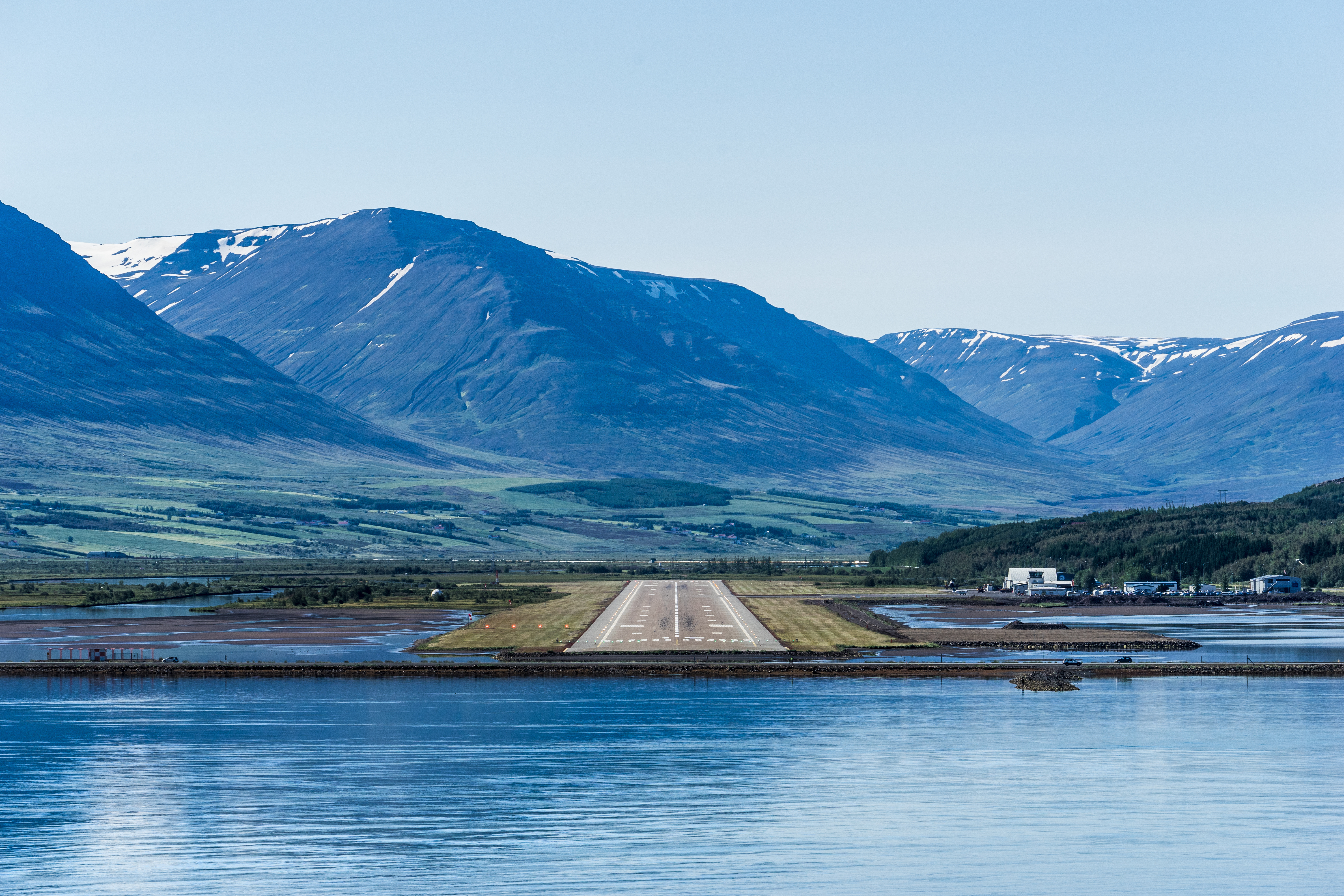 Akureyri Airport runway across Eyjafjörður with snow-capped mountains rising behind in summer light.