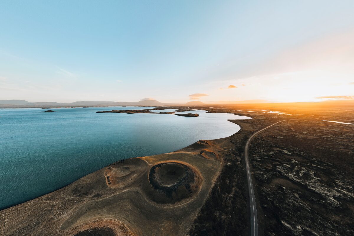 Aerial view of Lake Mývatn at sunset with Skútustaðagígar pseudocraters in the foreground and a road running east.