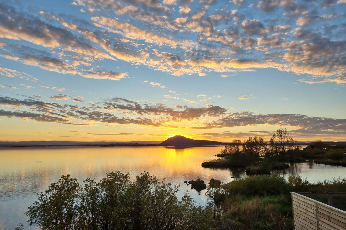 Golden sunset over Lake Mývatn with a mountain silhouette on the horizon and reflective water in the foreground.