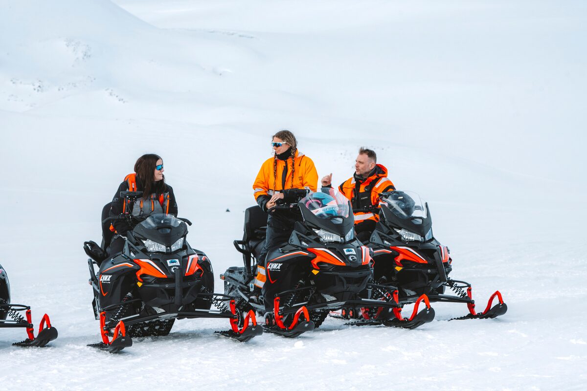 Three travelers in winter gear with snowmobiles on a glacier in Iceland.