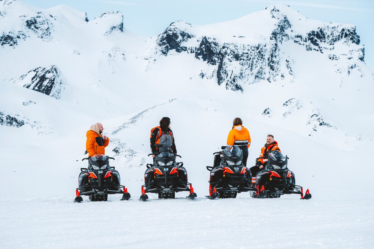 Four riders on snowmobiles paused on Langjökull glacier with mountains in the distance. 