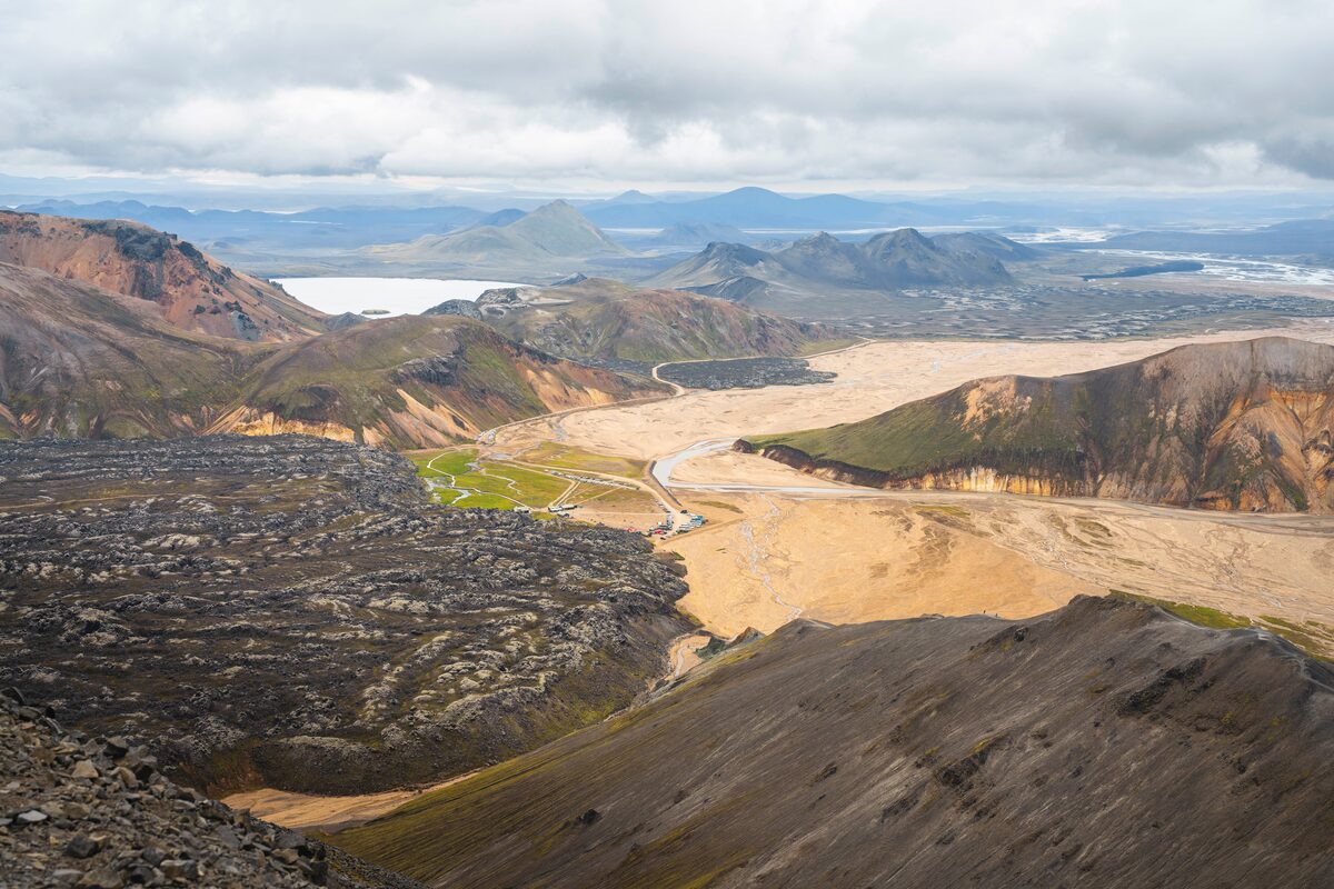 View from Bláhnúkur mountain over Landmannalaugar's sandy river plain, lava fields, and distant mountains. 