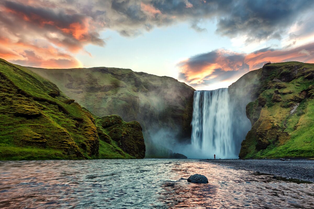 Skógafoss waterfall at sunset with a small figure at the base, South Iceland. 