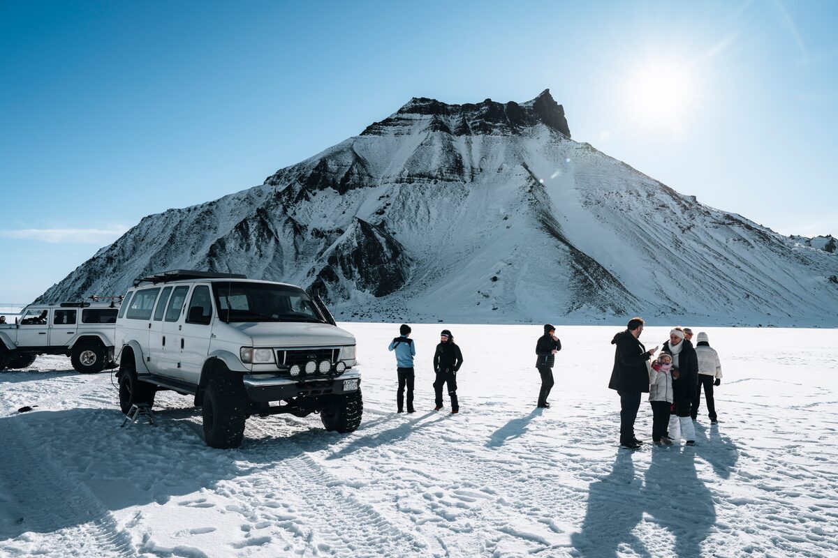 Super Jeep parked on snowfield beside Kötlujökull glacier with travelers gathered for Katla ice cave
