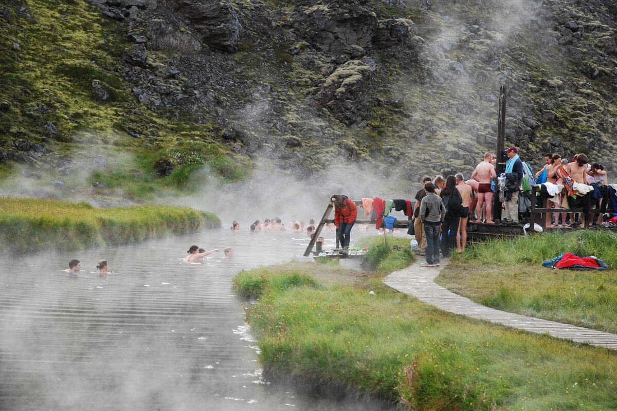 Bathers in the steaming pool and visitors with backpacks on the wooden deck at Landmannalaugar hot springs.