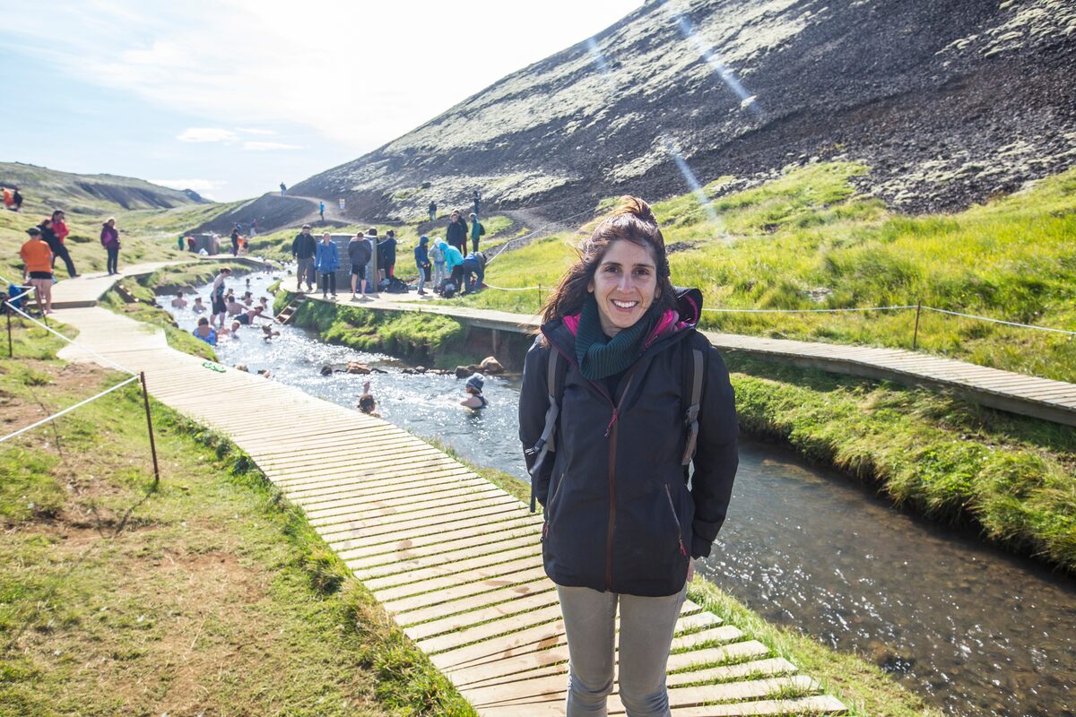 Visitor by the boardwalk with people bathing in the natural pool at Landmannalaugar, Iceland.