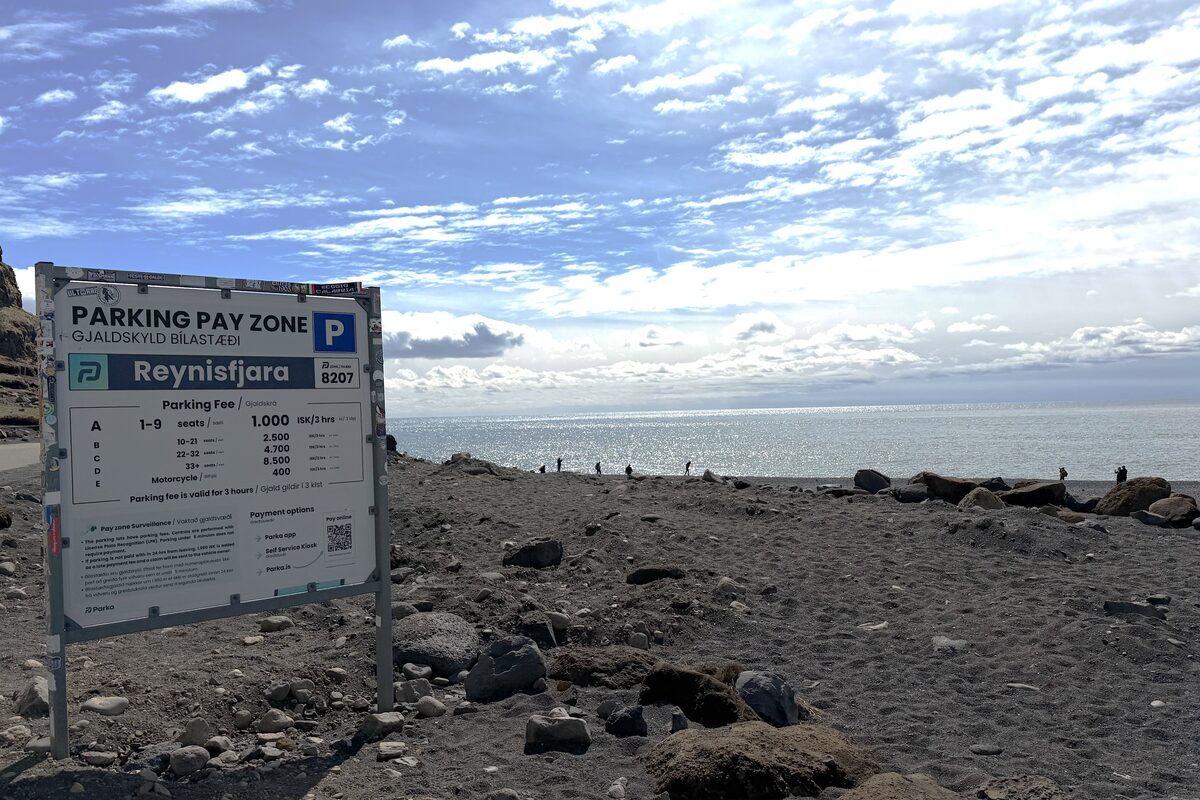Parking Pay Zone sign at Reynisfjara black sand beach with the ocean and cliffs behind.
