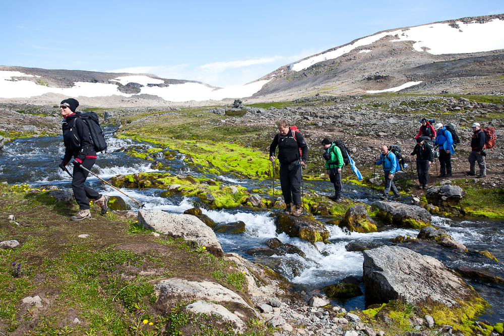 Hiking Group Wading Through Rocky River in Iceland